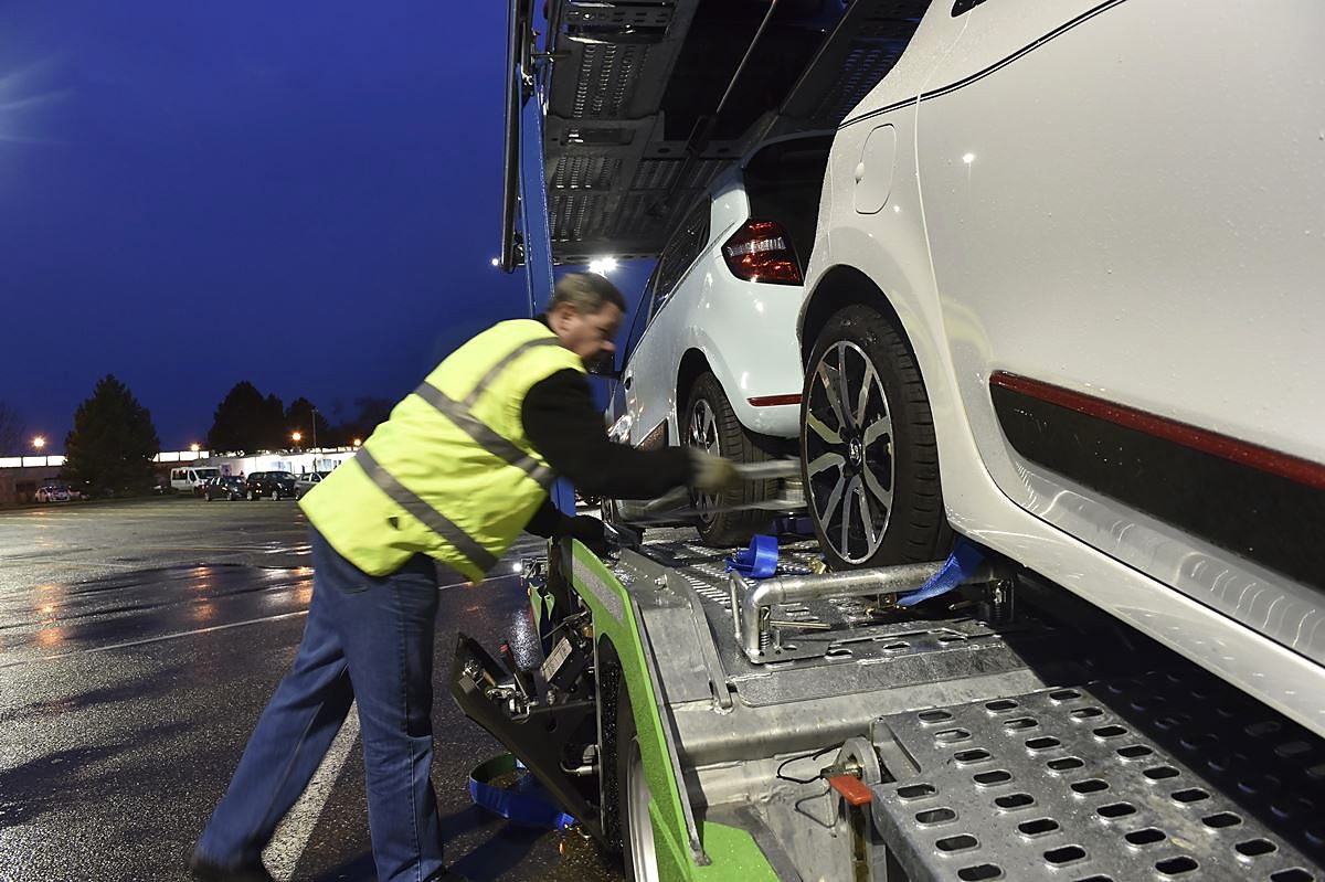 Un chauffeur arrime une voiture blanche sur un porte-voitures, de nuit
