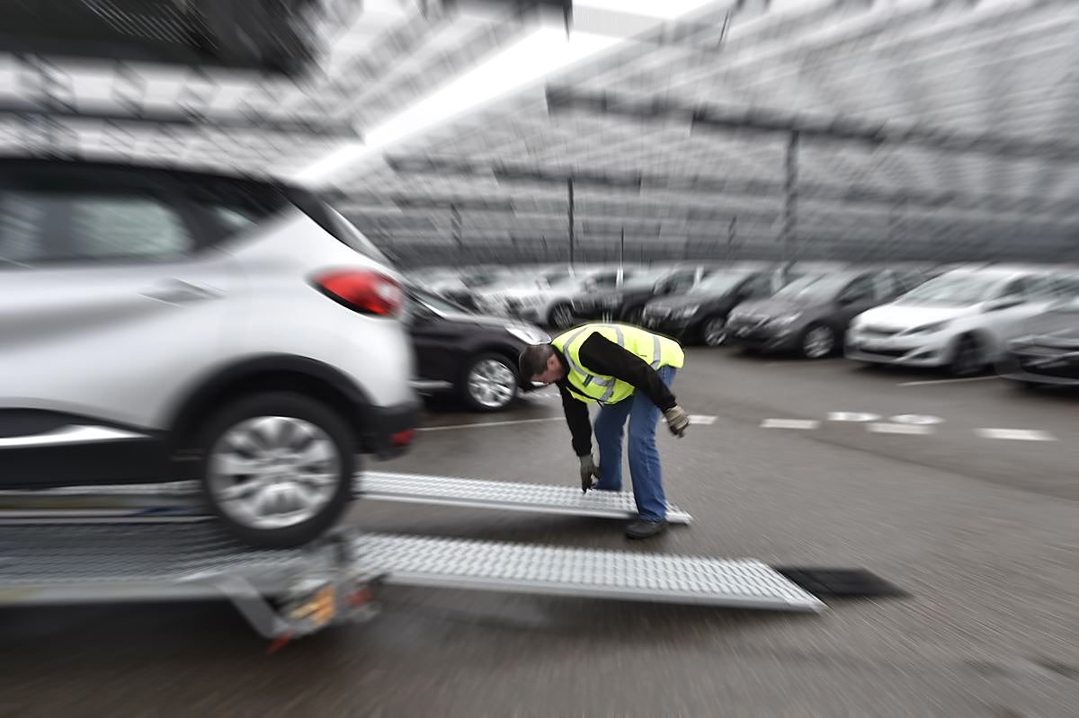 Un chauffeur au pied des rampes d'un porte-voitures, voitures en mouvement autour de lui